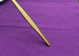 Close-up of the hammered textured tip of a gold flatware piece against a purple fabric background.