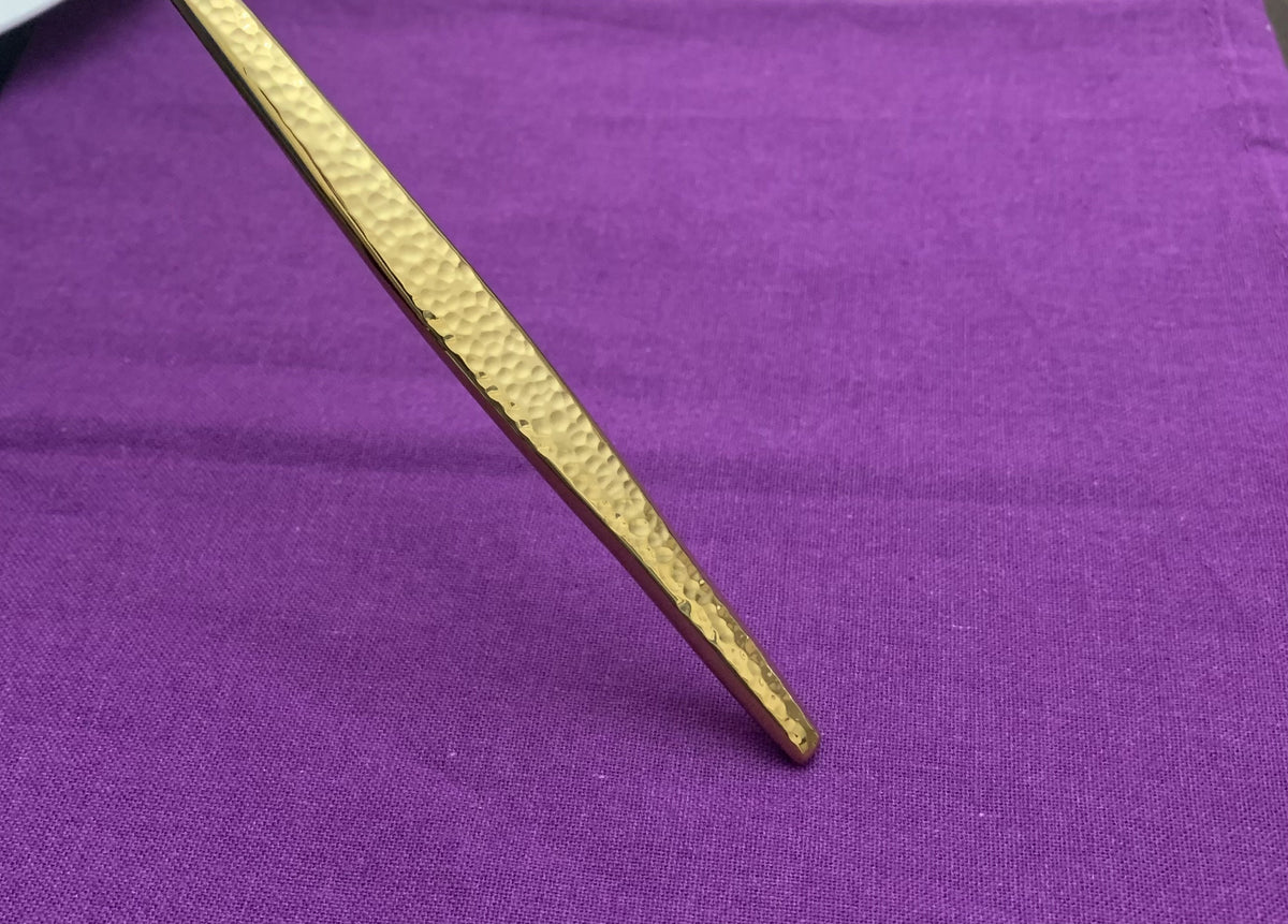 Close-up of the hammered textured tip of a gold flatware piece against a purple fabric background.