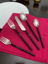 Five-piece stainless steel flatware set with black twisted swirl handles arranged on a red cloth napkin beside a white plate on a dark wooden table.