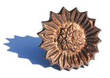 Bronze-toned metal sunflower-shaped napkin ring with textured petal and detailed seed pattern casting, casting a sharp shadow to the side.