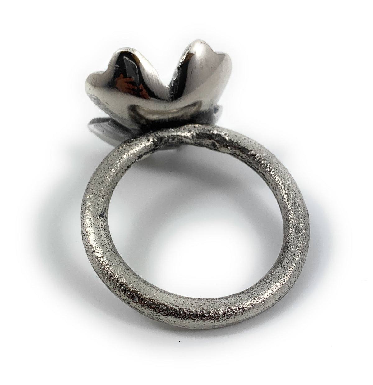 Silver-toned metallic napkin ring with textured circular band and a stylized flower-shaped top accent, photographed on a white background.