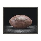 Close-up of a weathered vintage brown leather football resting on a dark wooden surface with a black background, framed in dark wood.