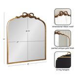 Arched mirror with painted antique gold frame featuring a dimensional ribbon motif at the top and D-ring hangers on the back, measuring 30" high by 28" wide.