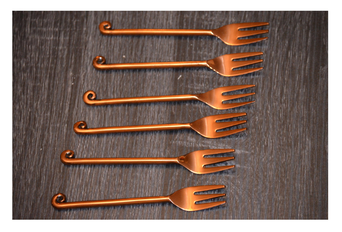 Set of five copper-finish appetizer forks arranged parallel on a dark textured surface, each featuring a distinctive curled handle end.