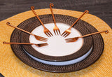 Set of six Vibhsa copper finish appetizer forks arranged on fabric with dark rose gold polish