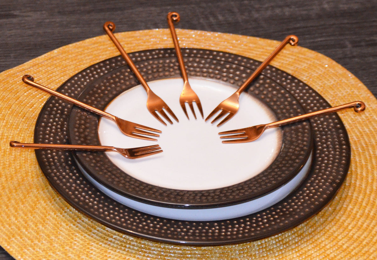 Set of six Vibhsa copper finish appetizer forks arranged on fabric with dark rose gold polish