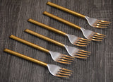 Set of six dinner forks with golden handles and polished silver fork heads arranged diagonally on a dark textured wooden surface