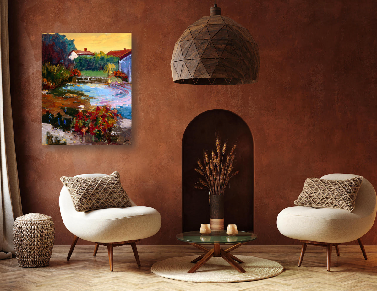 Cozy seating area with two cream-colored chairs featuring diamond-patterned pillows, a round glass coffee table, and a colorful impressionist village pond painting on a terracotta wall.