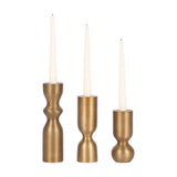 Set of three brass taper candle holders with varying sculpted shapes, each holding a white taper candle, arranged side by side on a white background.
