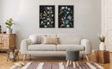 Two framed canvas art pieces depicting stylized blue and green foliage on black backgrounds, hung above a light gray sofa with textured pillows in a neutral-toned living room.