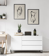 Two minimalist line art prints in black frames, one of an abstract face and the other a nude female body, mounted above a white modern dresser with plants and decor.