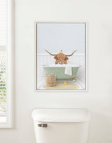 Framed canvas of a Highland cow with long horns in a clawfoot tub with a white towel, wicker basket, and rubber duck in a bright bathroom.