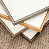 Four blank canvases with varying metallic and wooden frames—silver, gold, bronze with beaded detail, and dark wood—stacked on a textured beige patterned surface.