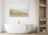 Minimalist bathroom with white freestanding oval tub and black faucet beneath a framed coastal landscape painting featuring soft dunes and calm sea under gray sky.