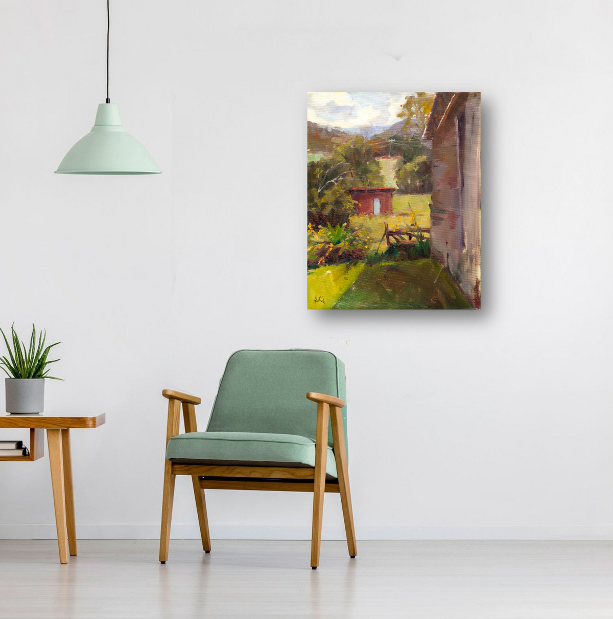 Impressionist-style canvas print of a garden shed with lush green foliage and a distant mountain under a partly cloudy sky, hanging on a white wall above a sage green armchair.