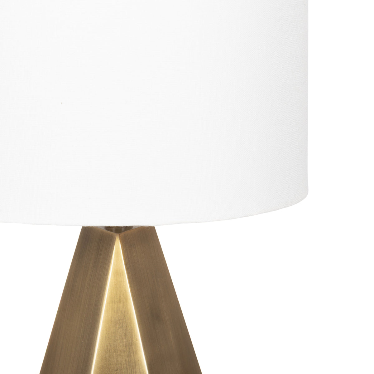 Close-up of a table lamp with a white cylindrical fabric shade and a bronze-colored, geometric triangular base
