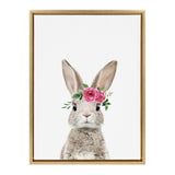Frontal portrait of a light brown rabbit wearing a pink rose and green leaf crown on its head, centered on a white background with a simple tan wooden frame.