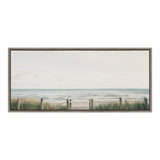 Framed canvas showing a pale sky over a calm beach with blue-gray ocean waves, green dune grasses, and a wooden post fence with rope barriers.