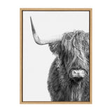 Black and white close-up of a Highland cow with shaggy hair covering its eyes and a prominent left horn, framed in light wood against a white background.