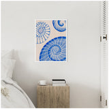 Framed canvas featuring three blue spiraled shell designs with white detailing on a pale beige background, hung on a white wall above a wooden side table.