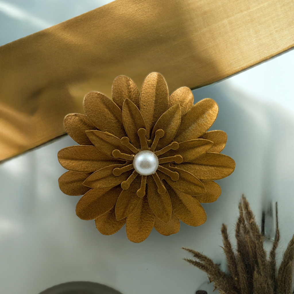 Textured golden floral napkin ring with layered petals and a central white pearl, paired with a matching golden fabric napkin on a white surface.