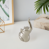 Silver elephant-shaped ring holder with multiple rings on its tail, placed on white surface