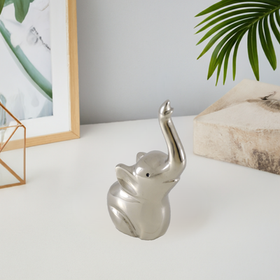 Silver elephant-shaped ring holder with multiple rings on its tail, placed on white surface