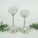 Set of two silver metal candle holders with spherical tops made of clear crystal-like beads arranged in a lattice, displayed against a plain white background with green foliage.