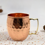 Single copper Moscow Mule mug with hammered surface texture and angular brass handle, placed on a light speckled fabric surface.
