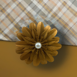 Golden flower-shaped napkin ring with layered petals and a central white pearl, holding a patterned plaid napkin in beige, gray, and yellow tones.