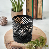 Two black votive candle holders with laser cut pattern casting shadows