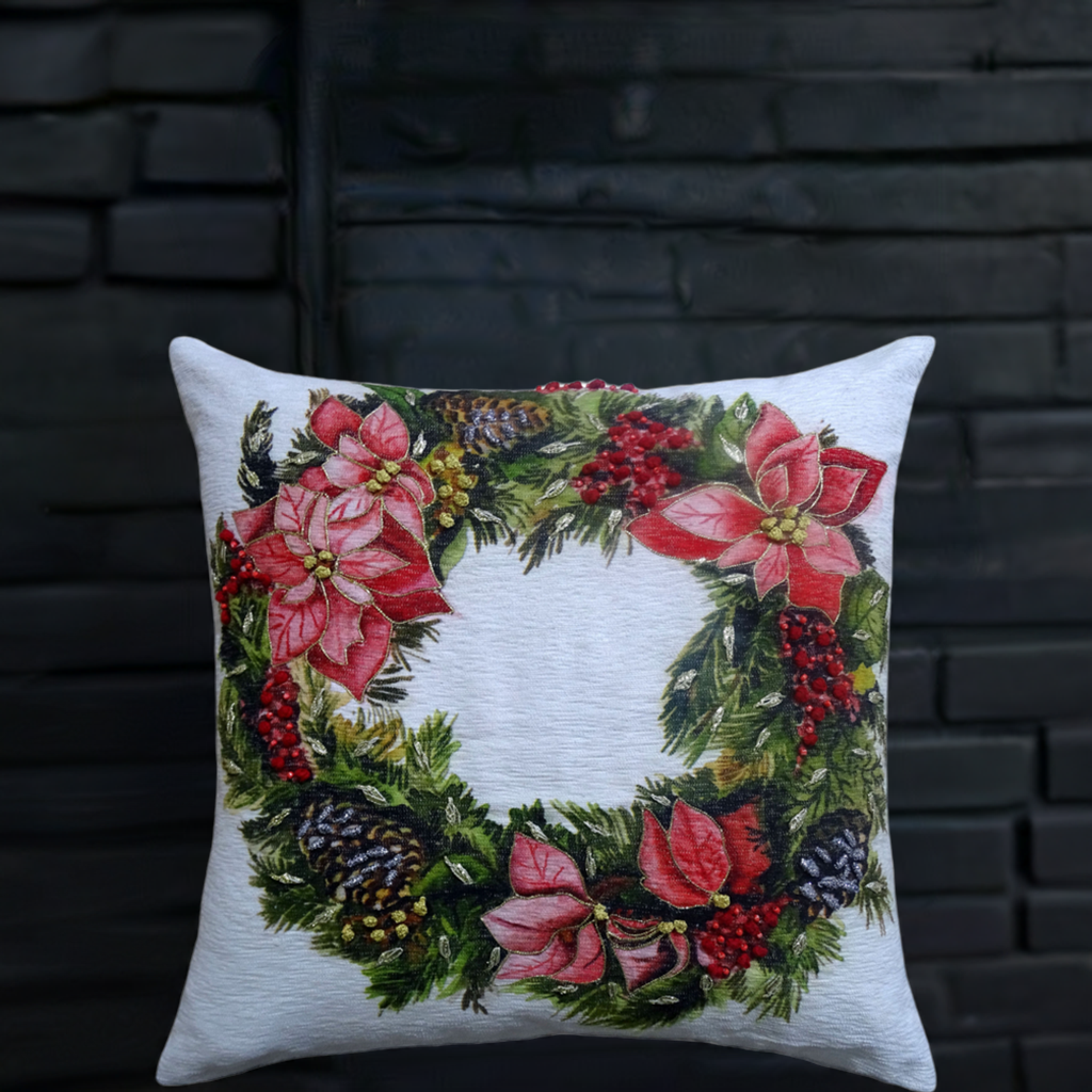 Square throw pillow with a Christmas wreath design featuring red poinsettias, pinecones, red berries, and green pine branches on a white background.