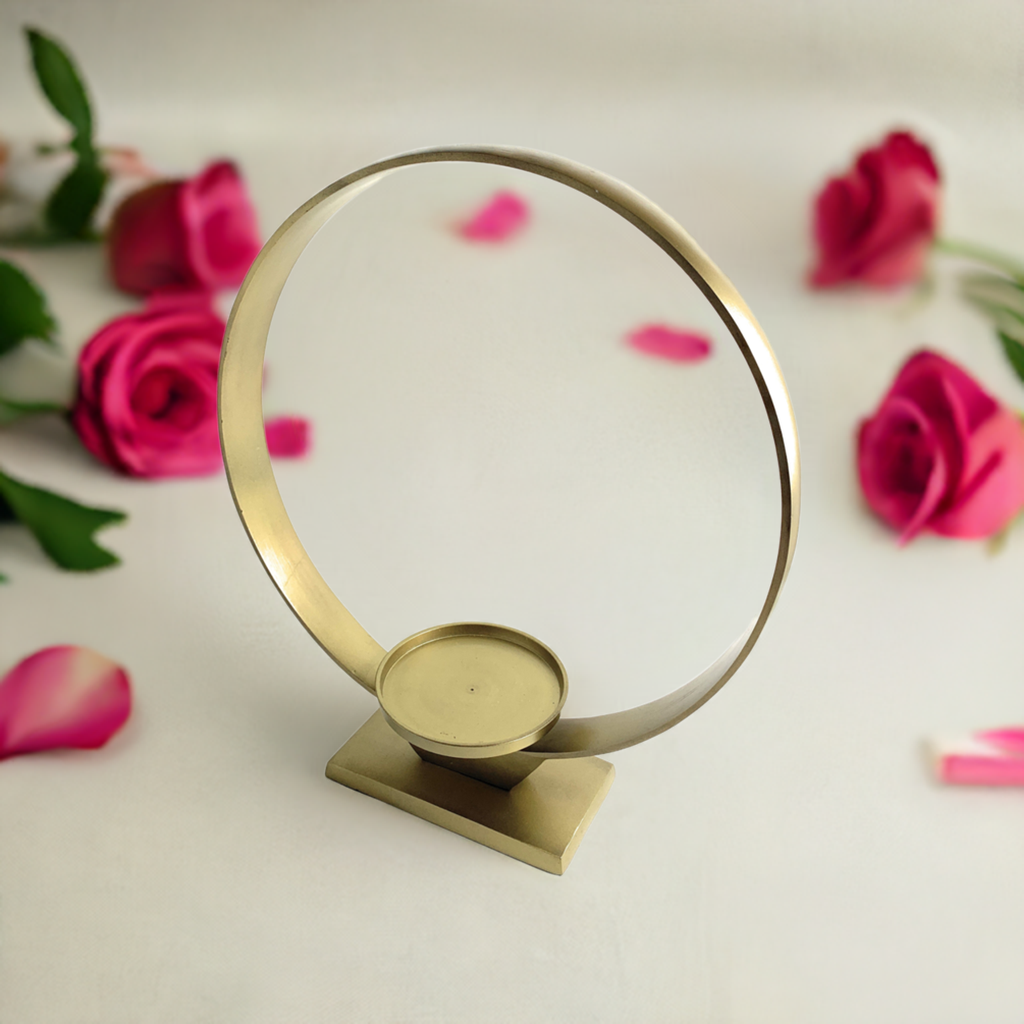 Circular golden metal candle holder with a flat base and a small round platform for the candle, surrounded by scattered pink rose petals on a white surface.