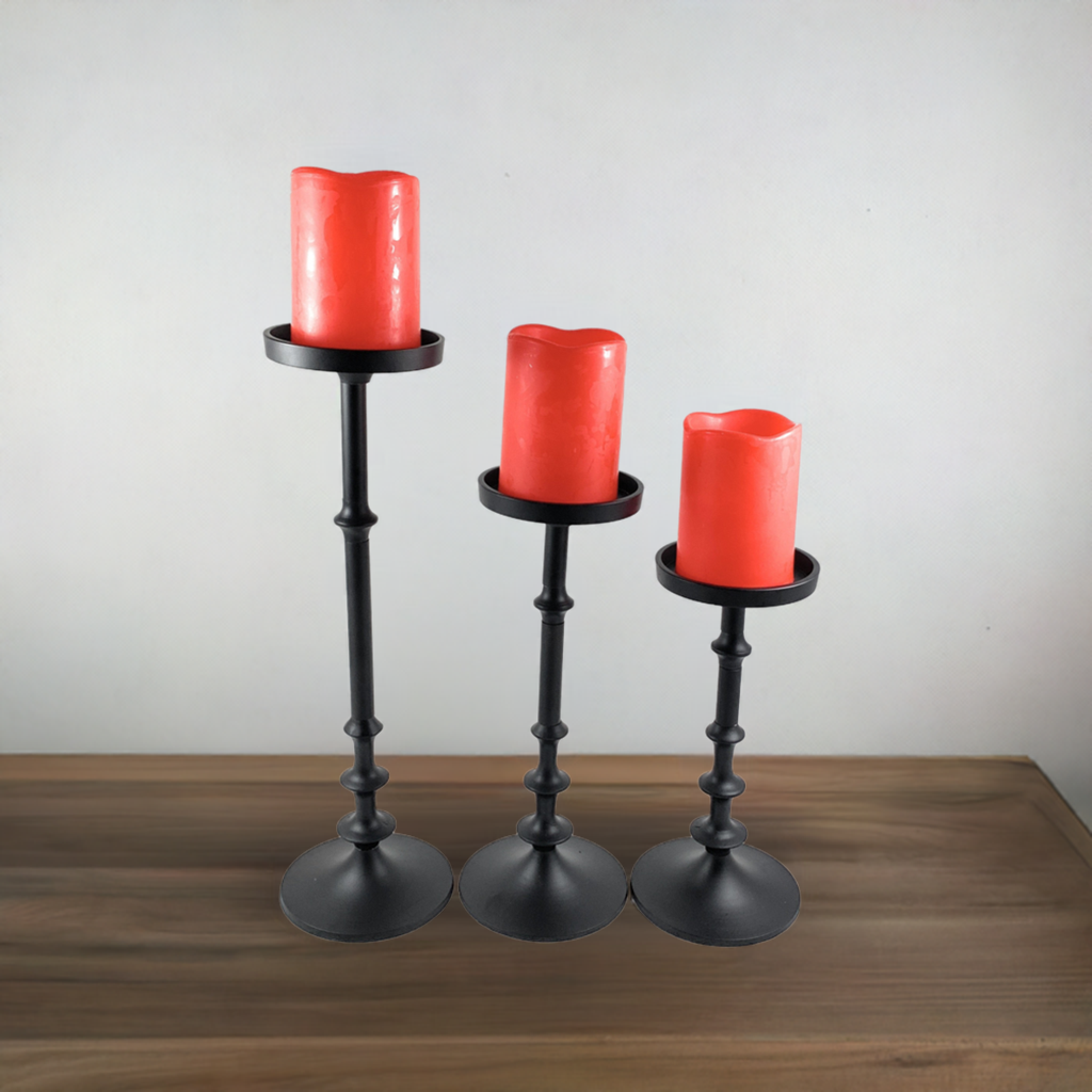 Set of three black metal candle holders with varying heights, each holding a thick red candle with slightly melted tops, displayed on a wooden surface against a plain background.