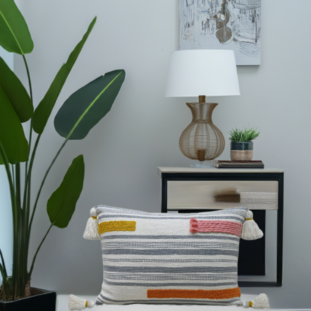 Decorative couch pillow with gray and white stripes, accented by mustard yellow, rust, and pink embroidery braids, featuring tassels on all four corners