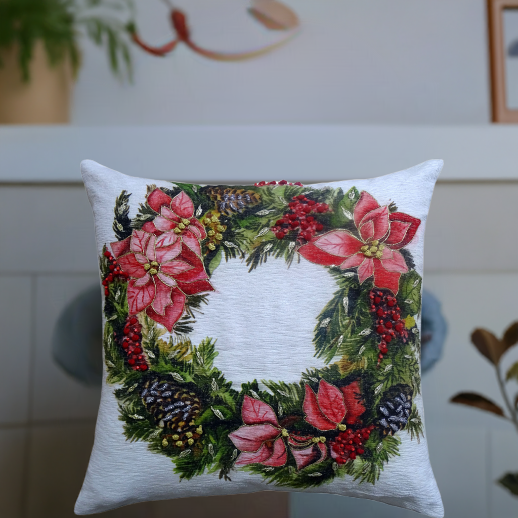 Square white throw pillow featuring a festive Christmas wreath design with red poinsettias, pinecones, and green foliage on the front center.