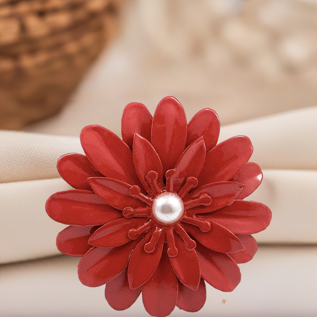 Red floral napkin ring with layered petals and a central white pearl, placed on a soft beige fabric background.