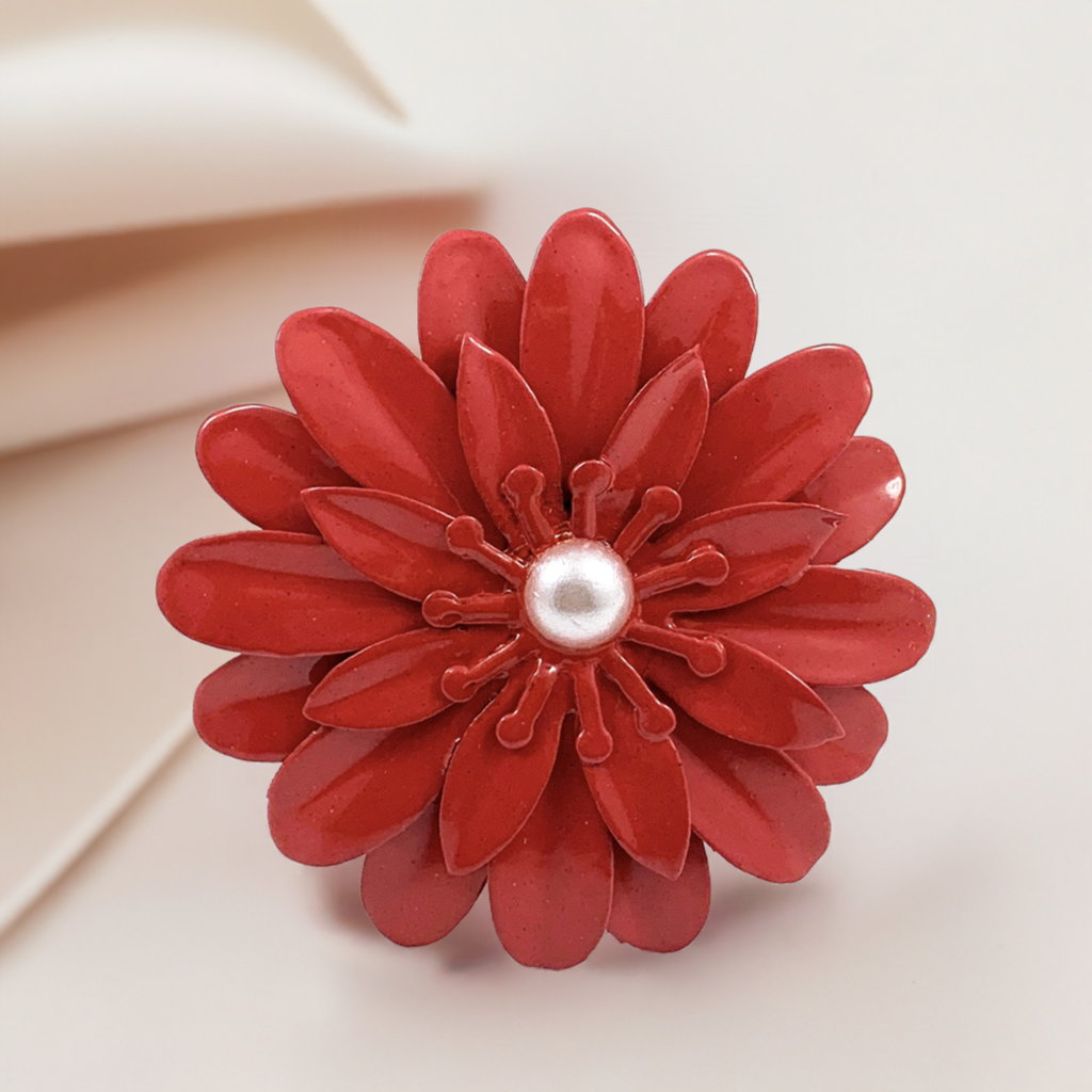 Red floral napkin ring with multiple petal layers and a central white pearl-like bead, displayed on a light beige background.