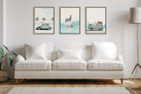 Three framed prints above a white sofa: left shows a green car with palm trees, center depicts a zebra surfing, right shows a white car with animals and luggage, all in soft pastel tones.
