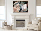 Abstract canvas with soft overlapping brushstrokes in blues, whites, and browns framed above a white fireplace in a beige-toned living room with armchair and baskets.