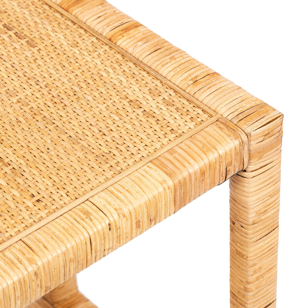 Close-up of a corner of a rectangle side table with woven rattan surface and rounded rattan-wrapped frame in natural beige tones.
