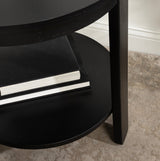 Close-up of the black round lower shelf of a wooden side table holding two stacked black books with white edges, standing on a textured beige carpet near a white wall.