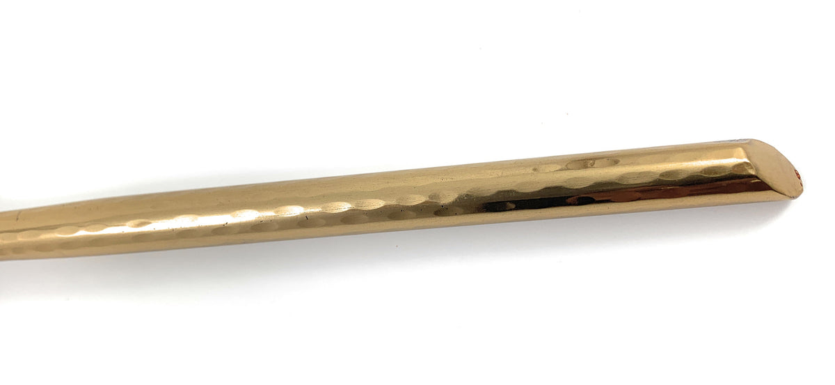 Close-up of a gold-toned metal utensil handle with a hammered texture and a rounded rectangular cross-section against a white background.