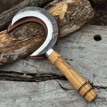 Hand-forged ritual witch sickle with crescent-shaped steel blade and wooden handle, including leather sheath