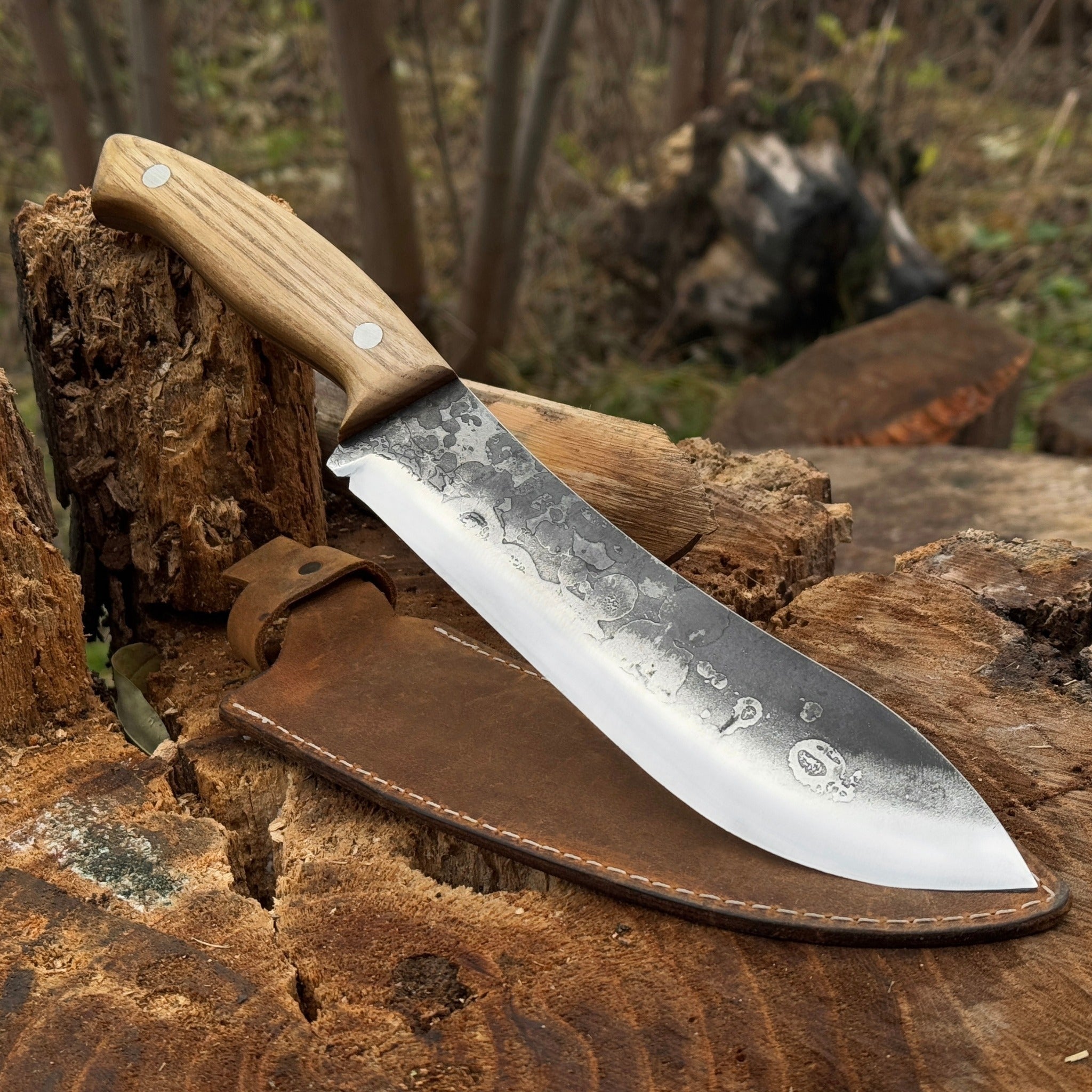 Hand-forged bushcraft knife with 17 cm carbon steel blade and ash wood handle, accompanied by leather sheath