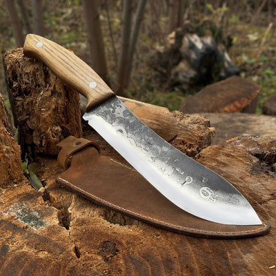 Hand-forged bushcraft knife with 17 cm carbon steel blade and ash wood handle, accompanied by leather sheath