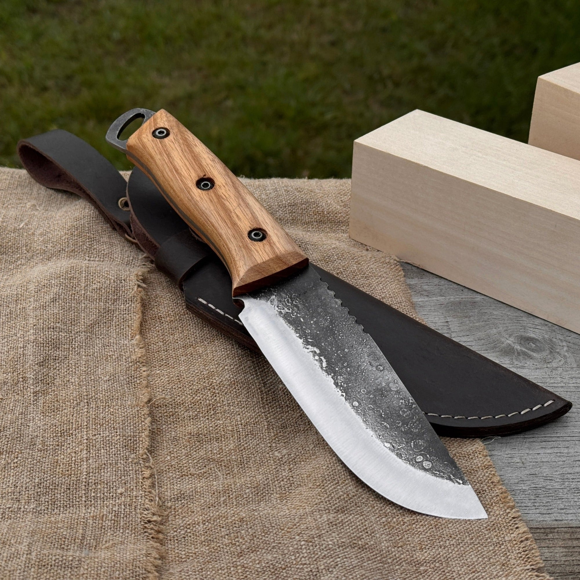 Hand-forged camping knife with 12.5 cm carbon steel blade and ash wood handle, with leather sheath