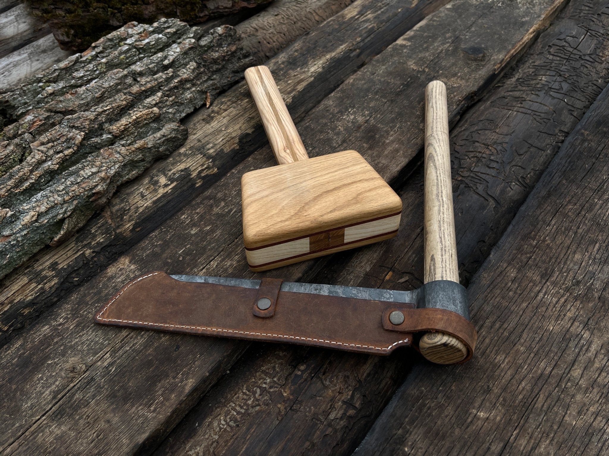 Hand-forged splitting froe with wooden mallet on wooden surface