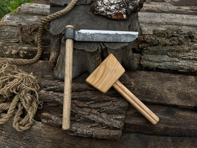 Hand-forged splitting froe with wooden mallet on wooden surface