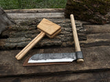 Hand-forged splitting froe with wooden mallet on wooden surface